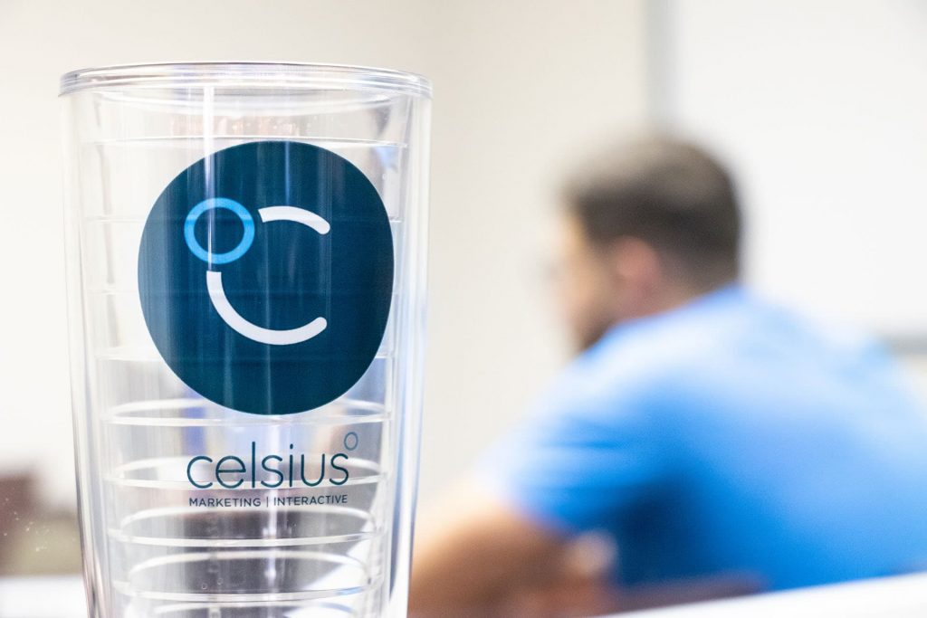 Photo of a Celsius-branded cup, with people meeting in the background.
