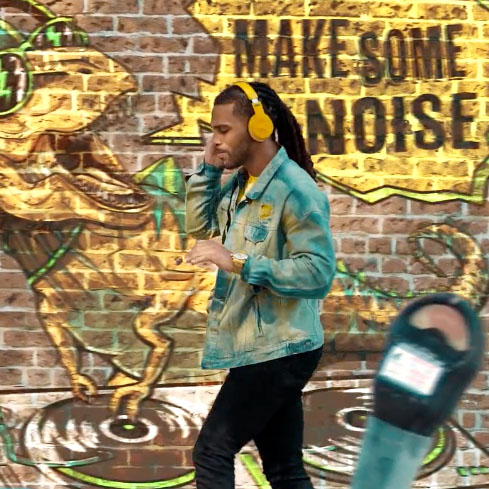 Young African American RMCAD student wearing headphones walking past brick wall with spraypainted artwork