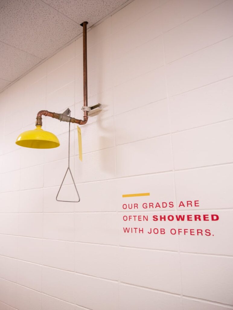 Wall graphic for ISU's Department of Civil, Construction and Environmental Engineering, featuring typography that declares, "Our grads are often showered with job offers," next to a safety shower station.