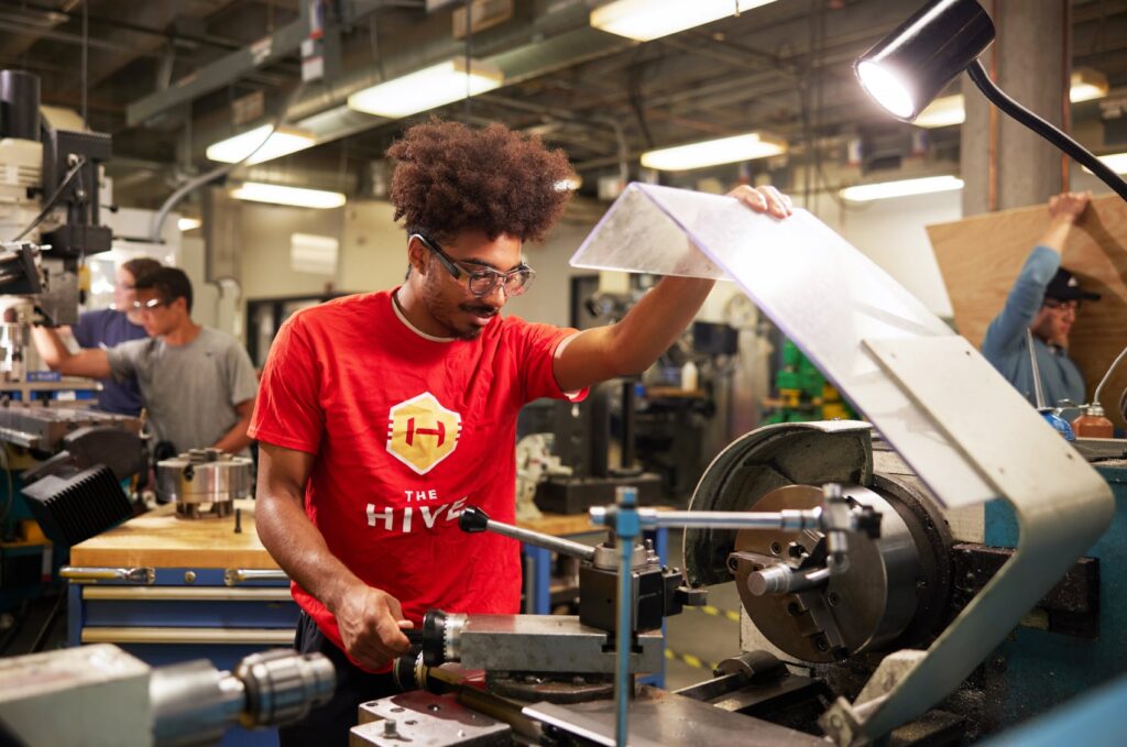 Photo of an ISU Mechanical Engineering student working hands-on with industrial equipment in The Hive, wearing a t-shirt featuring the logo.