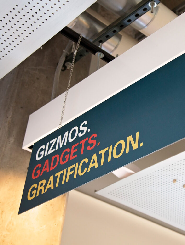 Directional sign in ISU's Department of Mechanical Engineering, declaring in bold typography, "Gizmos. Gadgets. Gratification."