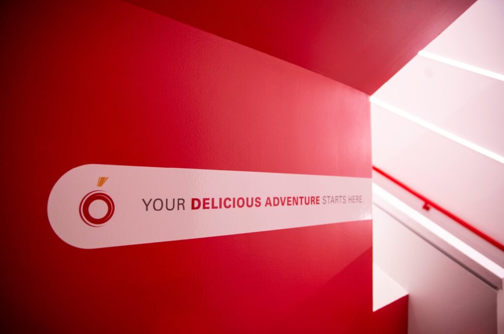 Environmental design in the stairwell leading up to The Mezzanine on ISU's campus, with the ISU Dining logo next to bold typography declaring, "Your delicious adventure starts here."