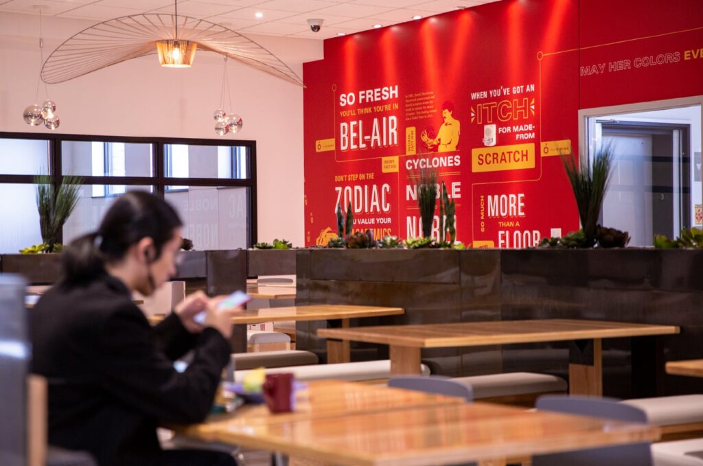 Environmental design of The Mezzanine on ISU's campus, featuring an area of tables for students to sit and eat lunch, with intricate yellow graphics on a red wall in the background.