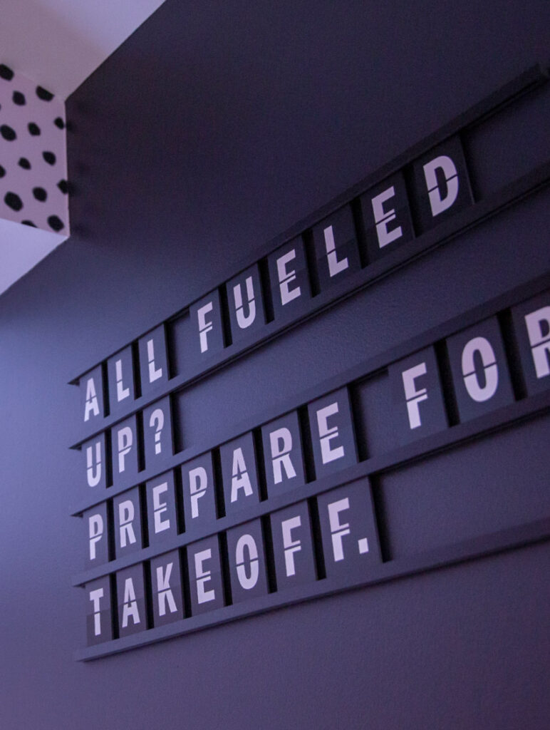 Wall art in The Roasterie, using flip letters to declare, "All fueled up? Prepare for takeoff."