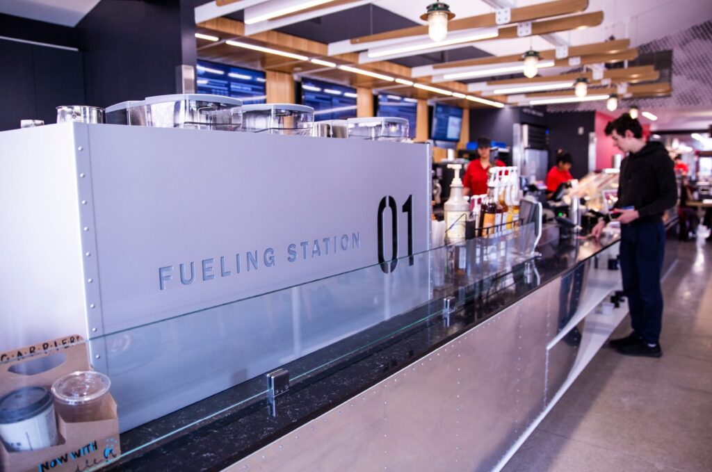 Restaurant design of The Roasterie coffee shop on ISU's campus, with a custom metal divider behind the espresso machine with die-cut lettering titling it as, "Fueling Station 01."