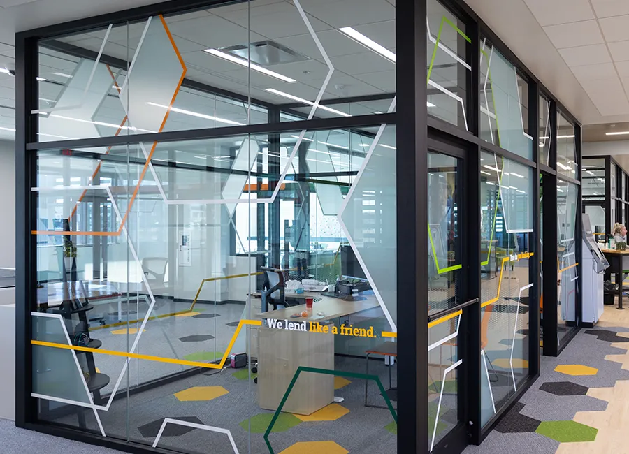 Office cubicle at Farmer's State Bank enclosed in glass, covered with hexagon decals and the tagline, "We lend like a friend."