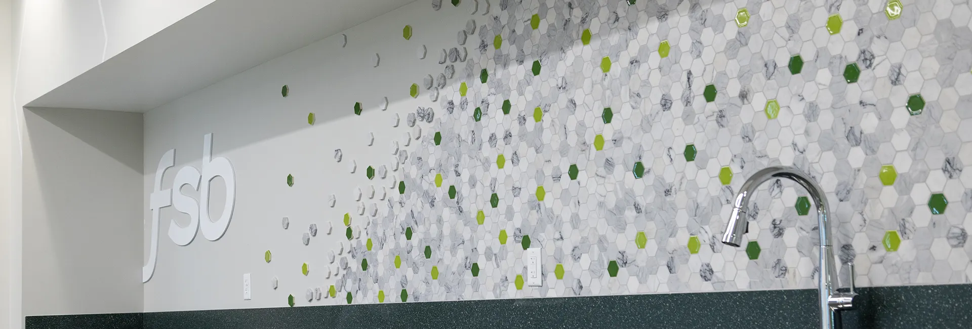 Hexagon-tile backsplash in the employee break room at Farmer's State Bank, featuring the brand's green colors and the logo in 3D acrylic letters.