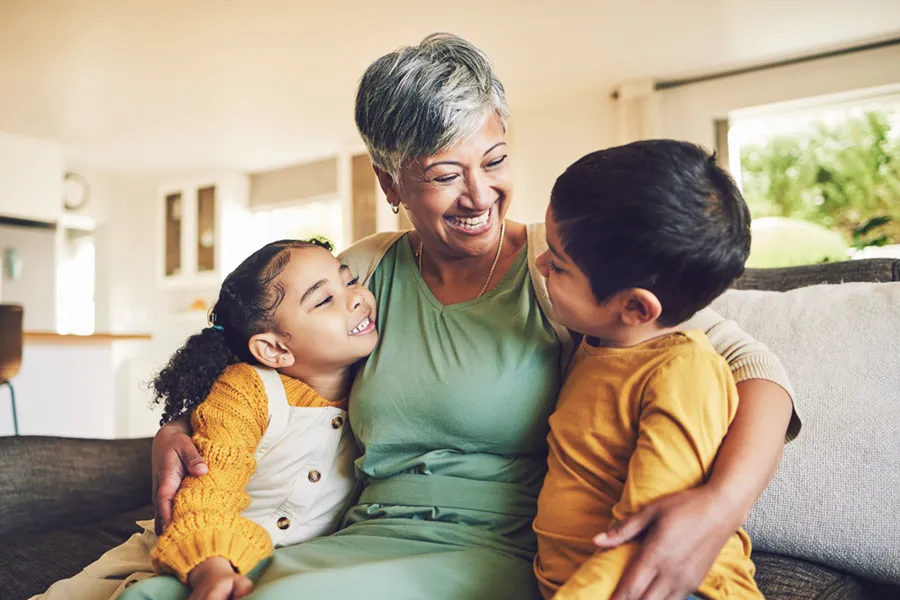 grandmother sitting on couch smiling and holding her grandchildren.