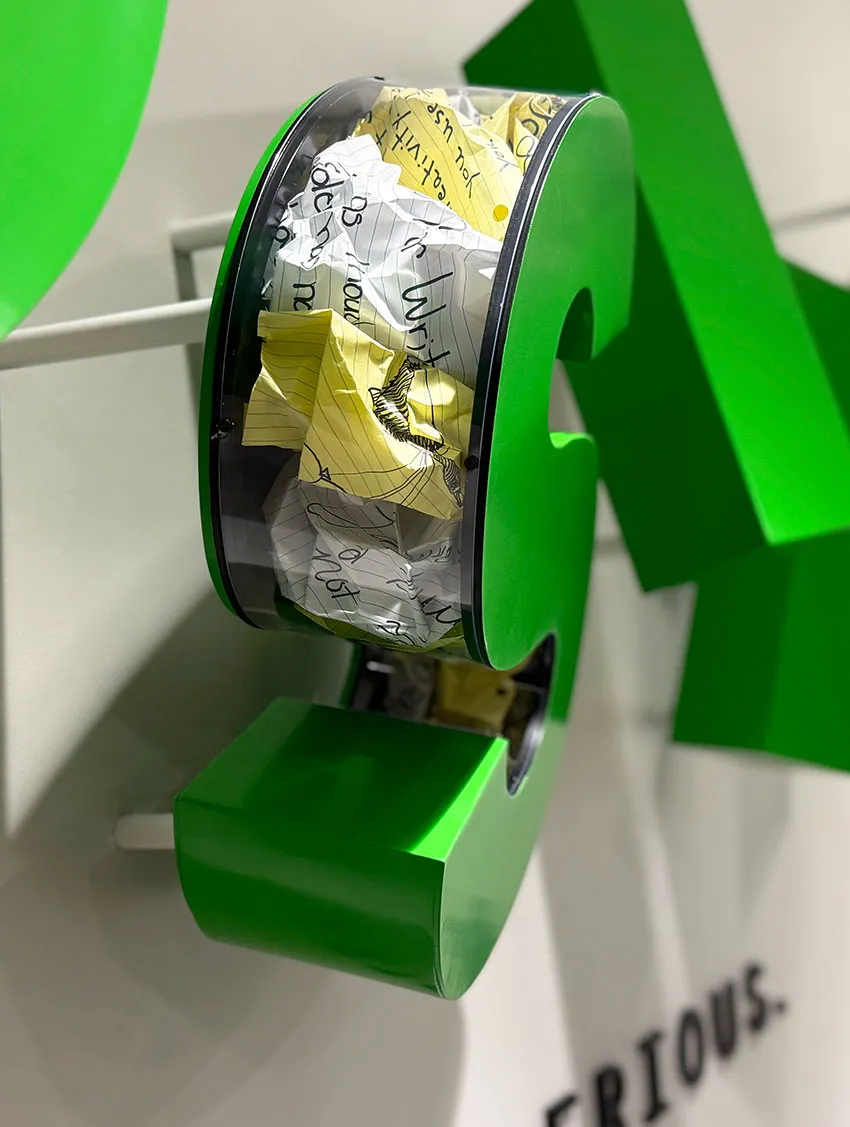Creative green question mark sculpture filled with crumpled papers on display in a modern art exhibit.