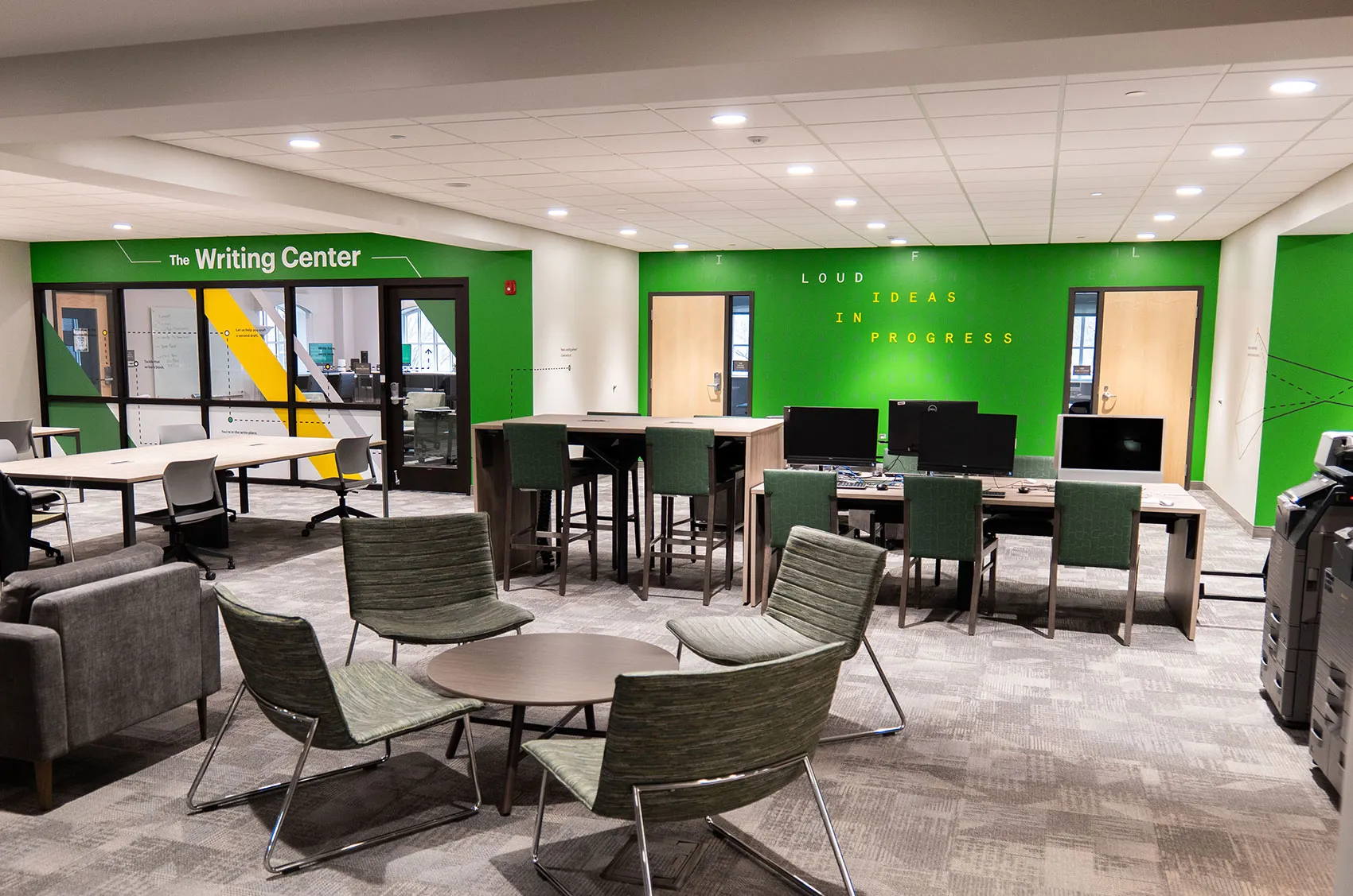 Modern writing center with green walls, seating, desks, and computers, showcasing a collaborative work environment.
